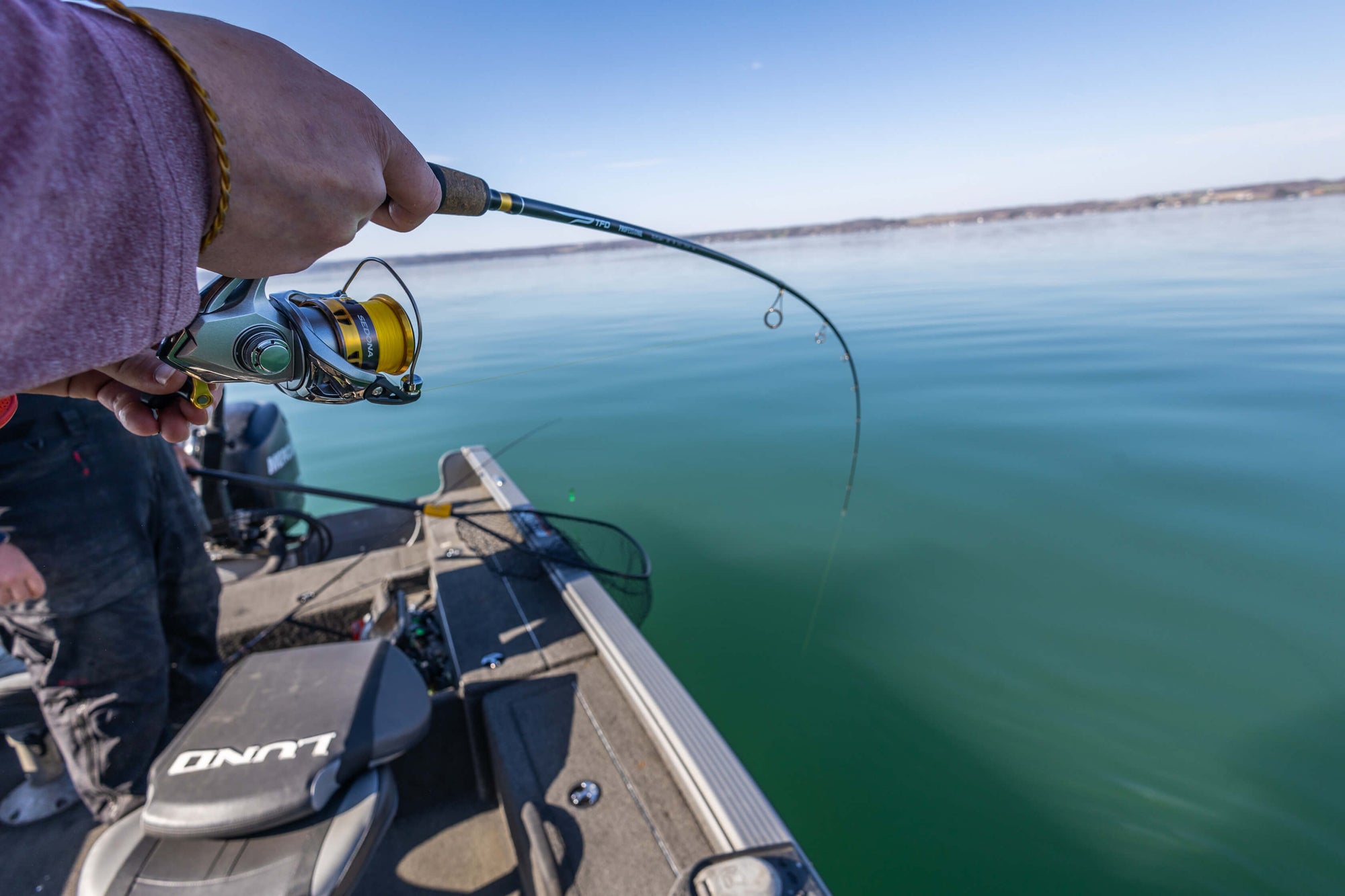 A pair of hands holding onto their fishing pole with the line in the water.