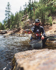 Fisherman kneeling in water, and holding onto a fish and fishing net