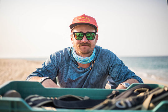 Christiaan staring at the camera with sunglasses and an orange hat. There is a body of water in the background