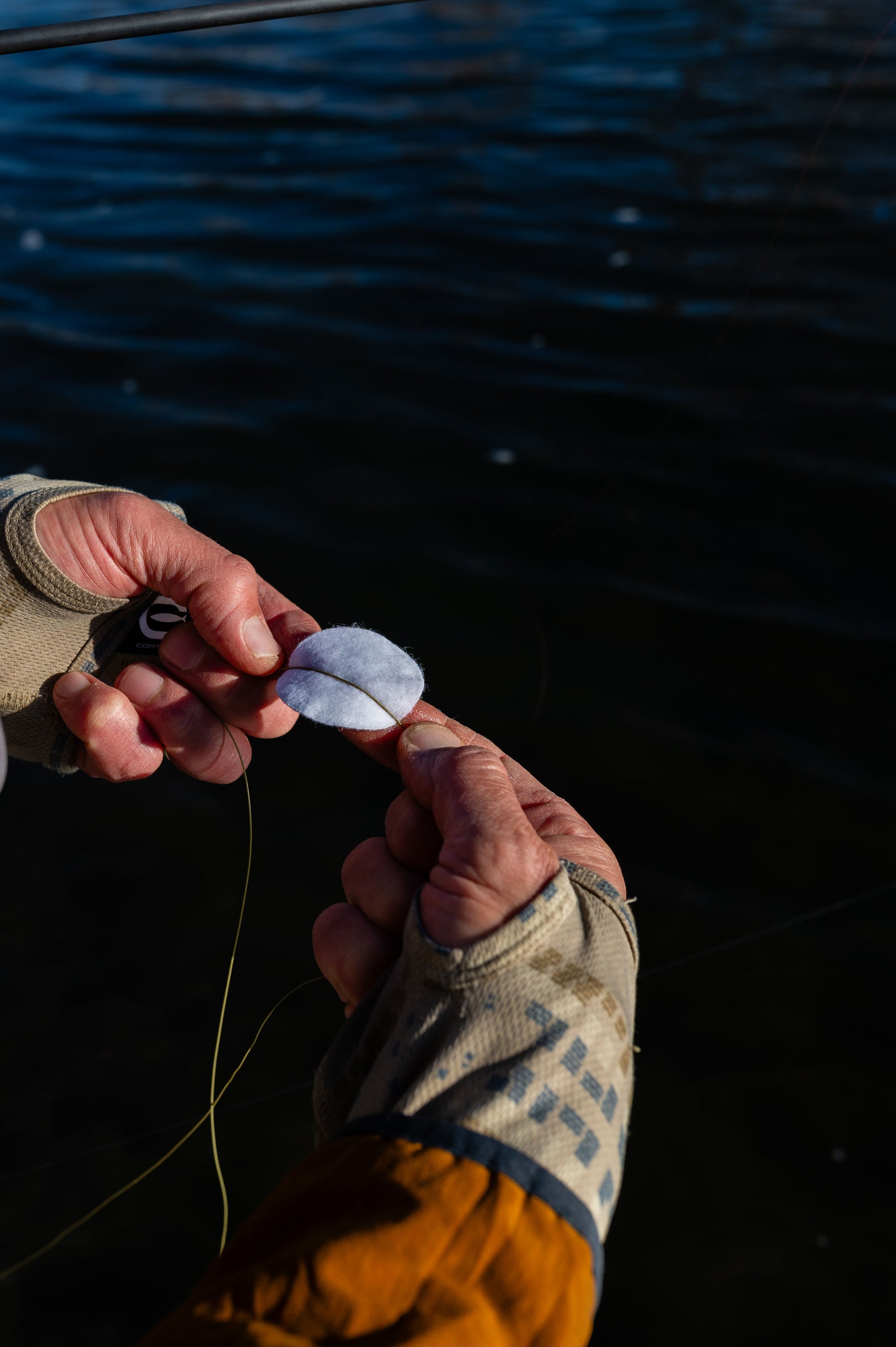 Close-up of hands using a lubricated pad to clean fly line with water in the background