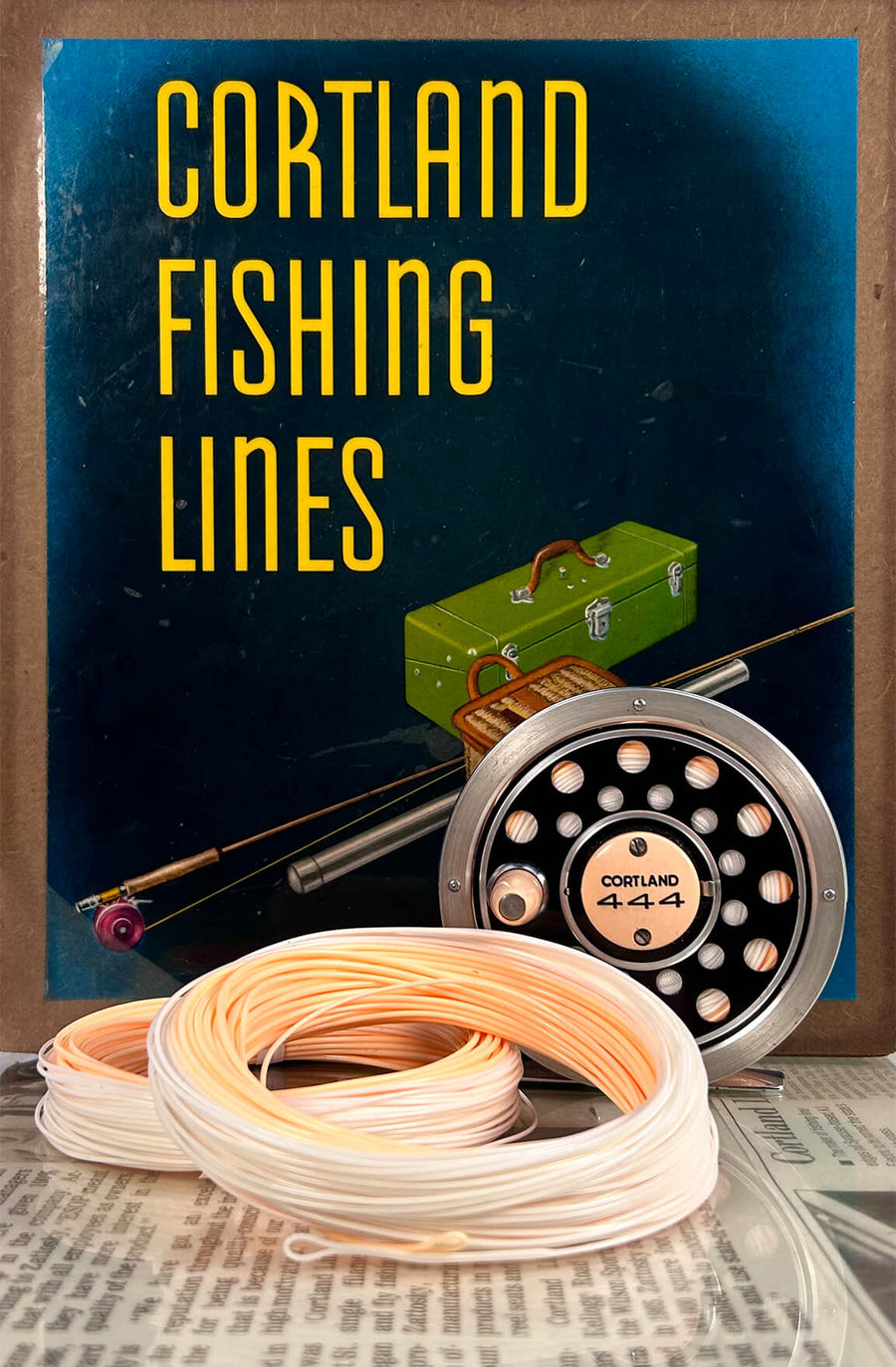 Two coils are in front and one is on a reel. Behind is a poster that says, Cortland Fishing Lines 