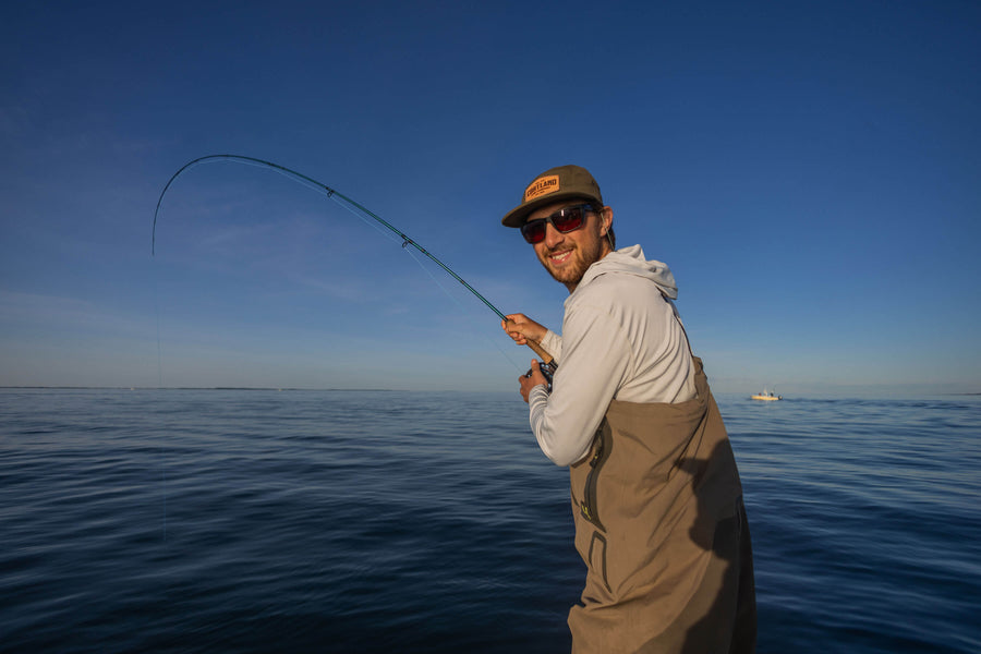 An angler is turning around and  smiling at the camera, while his fishing line is in the water. 