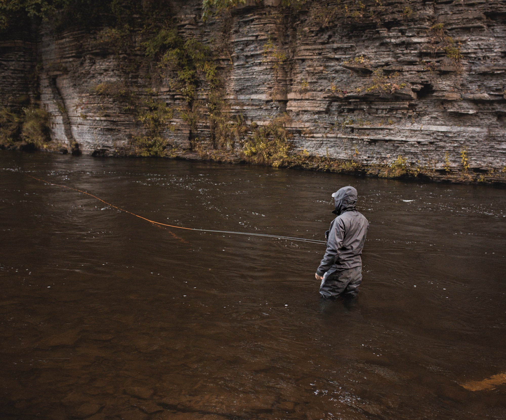 Someone standing in a flowing river with their back to the camera. They have a fly line in the water. 