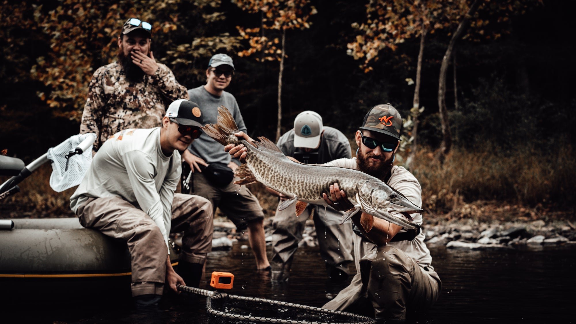 Three anglers look on as one is holding onto a pike. Another is seen bent over looking into a camera. 