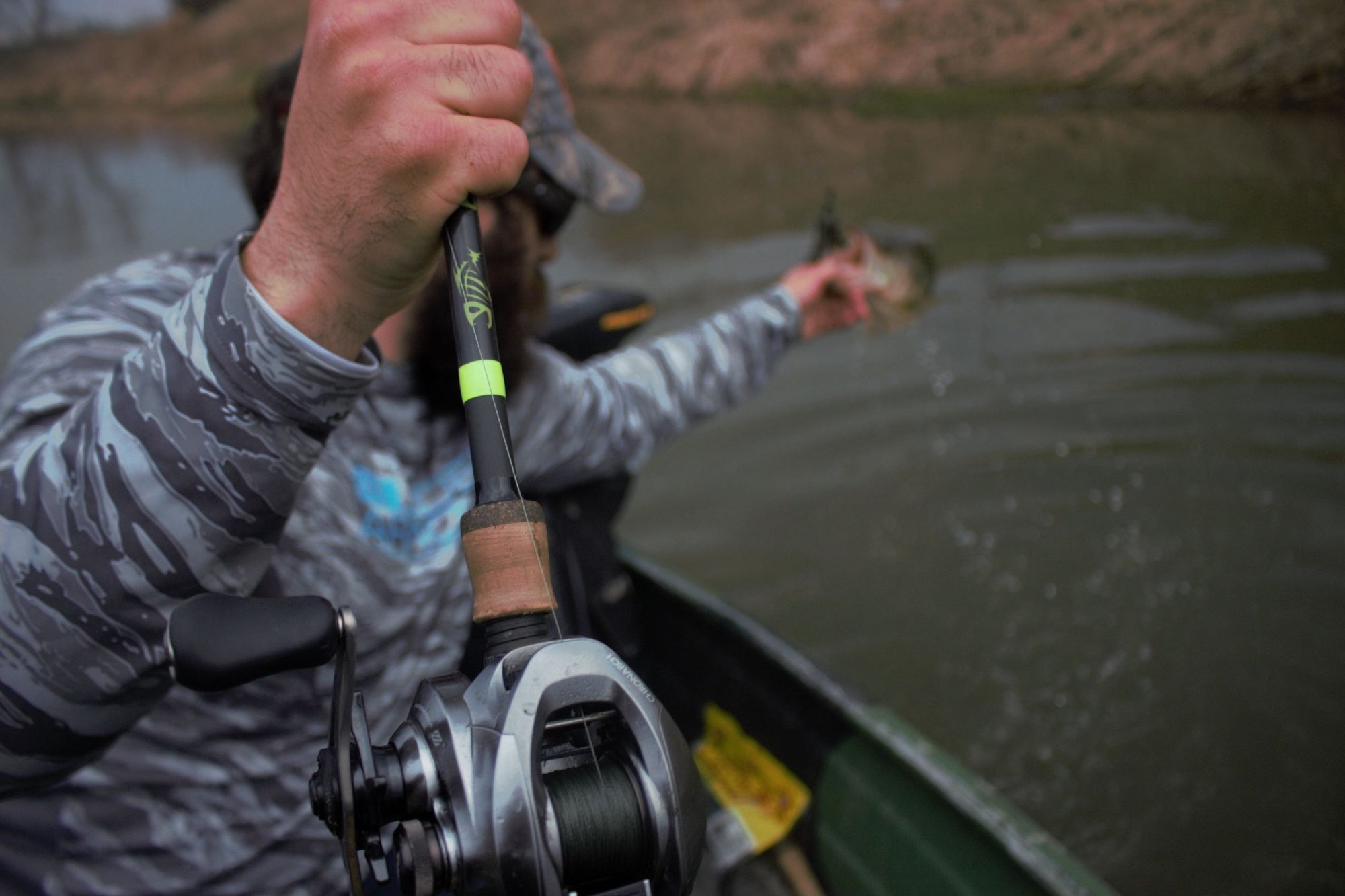 An angler is on a boat while holding a fish with one hand and their pole with another. 